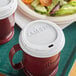 A white Cambro Sip Through Lid on a red and white Cambro insulated mug.