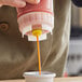 A person pouring yellow sauce into a cup.