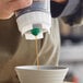 A San Jamar EZ-KLEEN 24 oz. sauce bottle with a small valve dispensing sauce into a bowl.