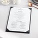 An Acopa black vinyl menu board on a table.