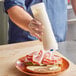 A person using a San Jamar sauce bottle to pour mayonnaise on a ham sandwich.