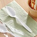 Two white Choice plastic spoons on a table next to a bowl of ice cream.