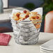 An American Metalcraft round chrome birdnest basket filled with food on a table.