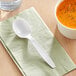 A white Choice plastic soup spoon on a napkin next to a bowl of soup.