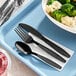 A tray with a bowl of broccoli and black utensils including a spoon and fork.