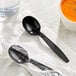 A black Choice heavy weight plastic soup spoon on a napkin.