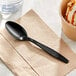 A black Choice plastic teaspoon on a napkin next to a cup of ice cream.