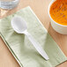 A white plastic soup spoon on a napkin next to a bowl of soup.