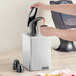 A person pouring liquid into a San Jamar countertop condiment dispenser.