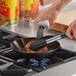 A person cooking food in a Choice carbon steel fry pan on a stove.