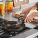 A person cooking steak in a Choice carbon steel fry pan on a stove.