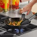 A person cooking food in a Choice carbon steel fry pan on a stove.