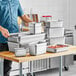 A man standing next to a stack of Choice stainless steel steam table pans.