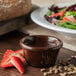 A brown Carlisle ramekin filled with chocolate sauce next to a salad.