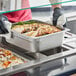 A person in gloves holding a stainless steel tray of food with meat and vegetables.