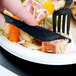 A person cutting food with a WNA Comet Classicware EcoSense black plastic knife.