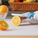 A hand holding a Choice blue serrated utility knife cutting an orange.