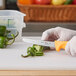 A hand in a glove cutting a green pepper with a Choice serrated utility knife.