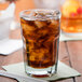 A close-up of an Anchor Hocking New Orleans beverage glass filled with brown liquid and ice.