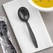 A black plastic spoon wrapped in a plastic bag on a napkin next to a bowl of soup.