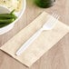 A white heavy weight plastic fork on a napkin next to a bowl of green beans.