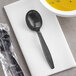 A black plastic wrapped soup spoon on a napkin next to a bowl of soup.