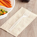A clear plastic Choice fork on a napkin next to a bowl of carrots and corn.