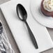 A black plastic wrapped Choice teaspoon on a white napkin next to a chocolate cake.