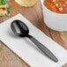 A black Choice heavy weight plastic soup spoon on a napkin next to a bowl of soup.