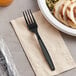 A black plastic wrapped fork on a table next to a plate of food.