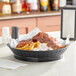 A Tablecraft black plastic diner platter in a restaurant serving basket on a table.