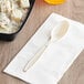 A beige plastic spoon next to a bowl of food.