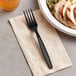 A black plastic Choice fork on a napkin next to a bowl of food.