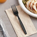 A black plastic wrapped fork on a table next to a plate of food.