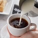 A person pouring Silk Original Almond milk into a cup of coffee.