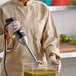A woman in a chef's coat using a Waring immersion blender to mix liquid in a bowl.