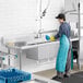 A person in a blue apron washing dishes in a professional kitchen at a Regency dishtable.
