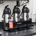 A Bunn Universal Airpot Rack holding three stainless steel coffee containers on a counter.