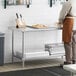 A man in an apron standing next to a Regency stainless steel work table with undershelf.