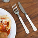 A plate of pasta with a WNA Comet Reflections Duet plastic knife and fork on a table.