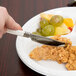 A hand holding a WNA Comet stainless steel look plastic knife over a plate of food.