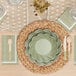 A table setting with a Sophistiplate Sage Scalloped Edge paper cocktail napkin, green bowl, and cutlery.