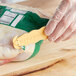 A person in a yellow glove using a yellow Klever Kutter to cut a plastic bag of food.
