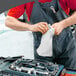 A man in overalls using a WypAll white wiper to clean a car engine.