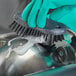 A person wearing gloves cleaning a metal object with a Carlisle Sparta black handheld scrub brush.