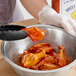 A gloved hand pouring Sweet Baby Ray's Hot Sauce onto a bowl of chicken wings.