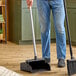 A man using a Carlisle black upright dustpan with a metal pole.