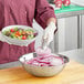 A person in a purple uniform using a Choice stainless steel mixing bowl to prepare a salad with tomatoes and carrots.