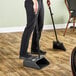 A man using a Carlisle lobby dustpan and broom to sweep the floor in a professional kitchen.