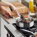 A person using a Vollrath stainless steel saute pan to cook vegetables on a stove.